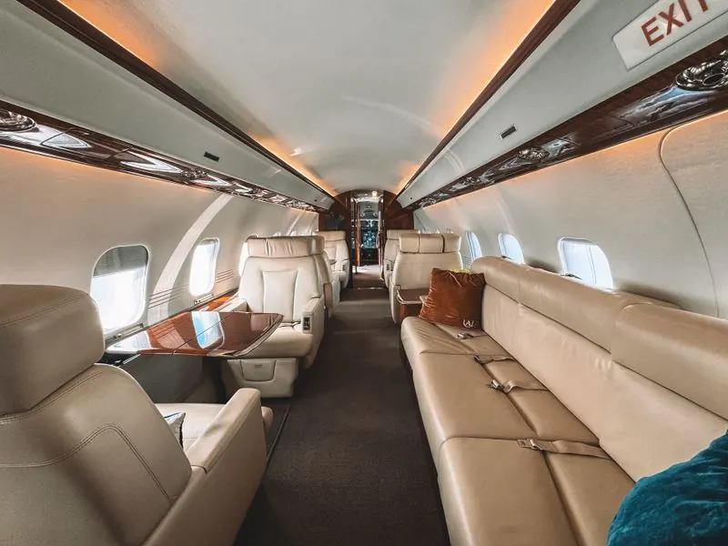 Private jet cabin interior with plush beige leather seats and polished wooden trim