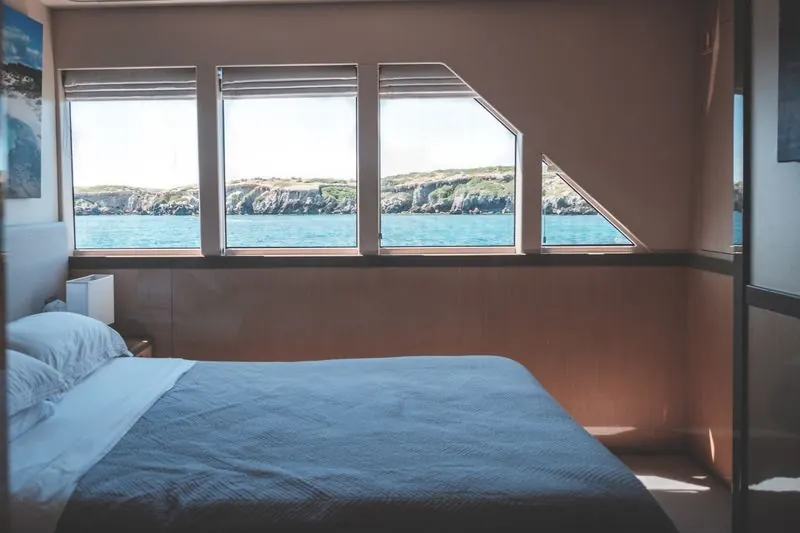 Modern yacht cabin interior with a comfortable bed and bright windows looking out to the sea